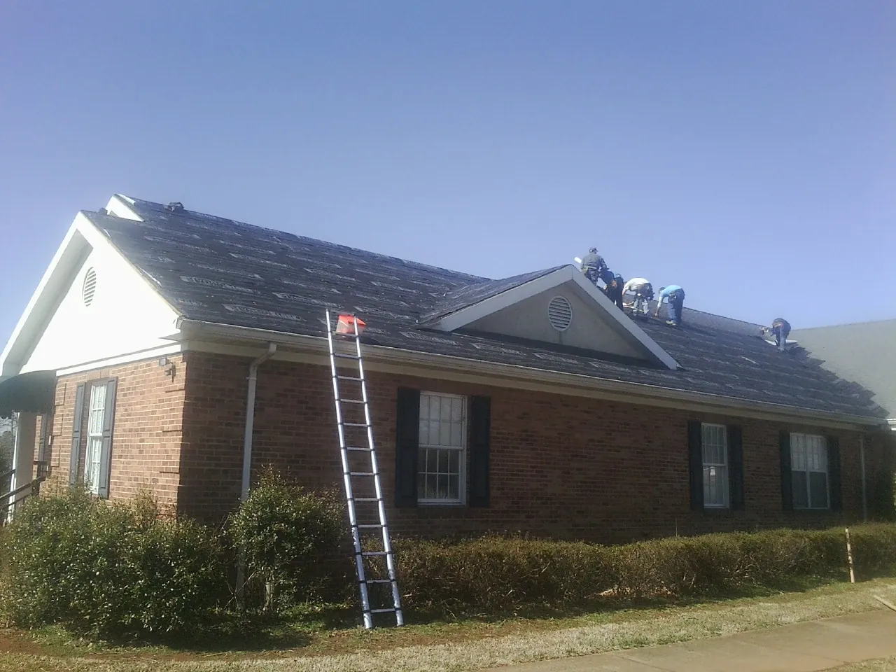 Crew tearing shingles off a brick ranch roof with a ladder set — Metal Roof Repair work by our crew in Moon