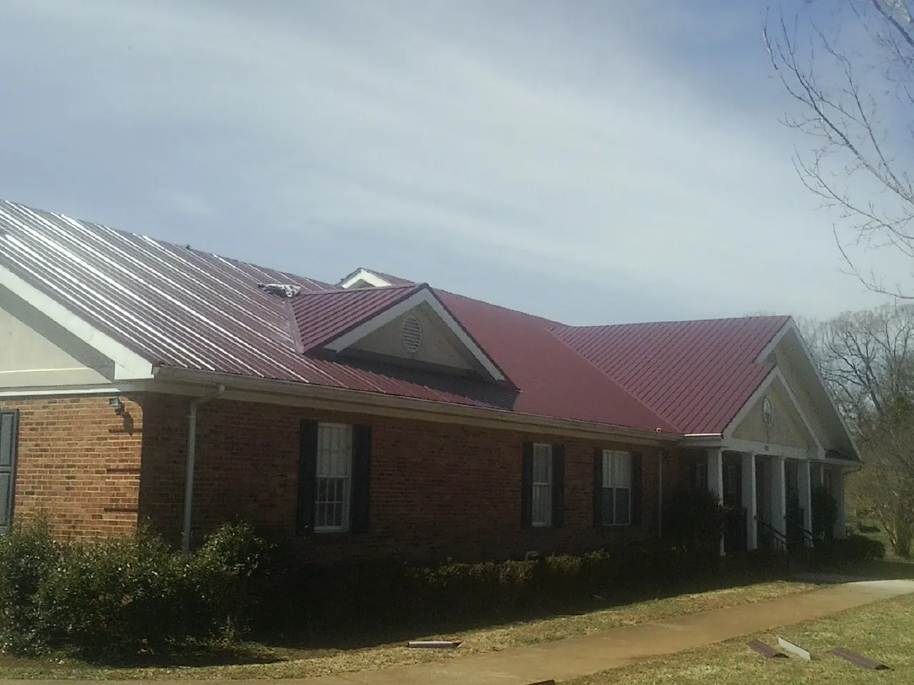 Red metal roof with gabled entries on a long brick building, from a Hail Damage Roof Repair job in Moon