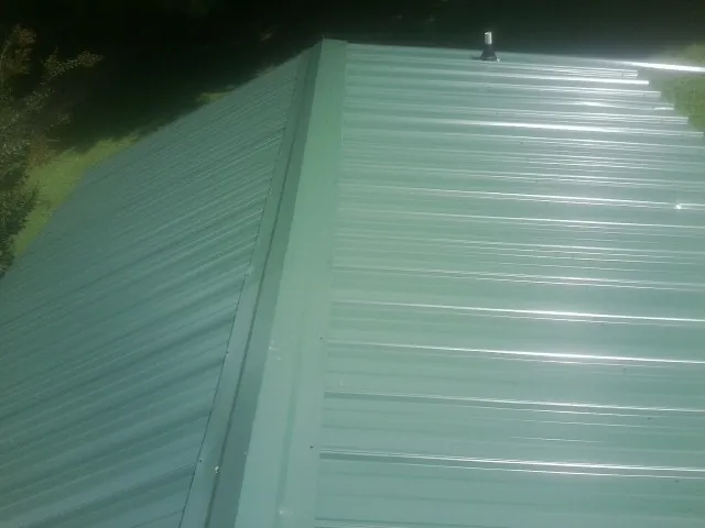 New green metal panels meeting at the ridge of a roof — Flat Roof Repair work by our crew in Moon
