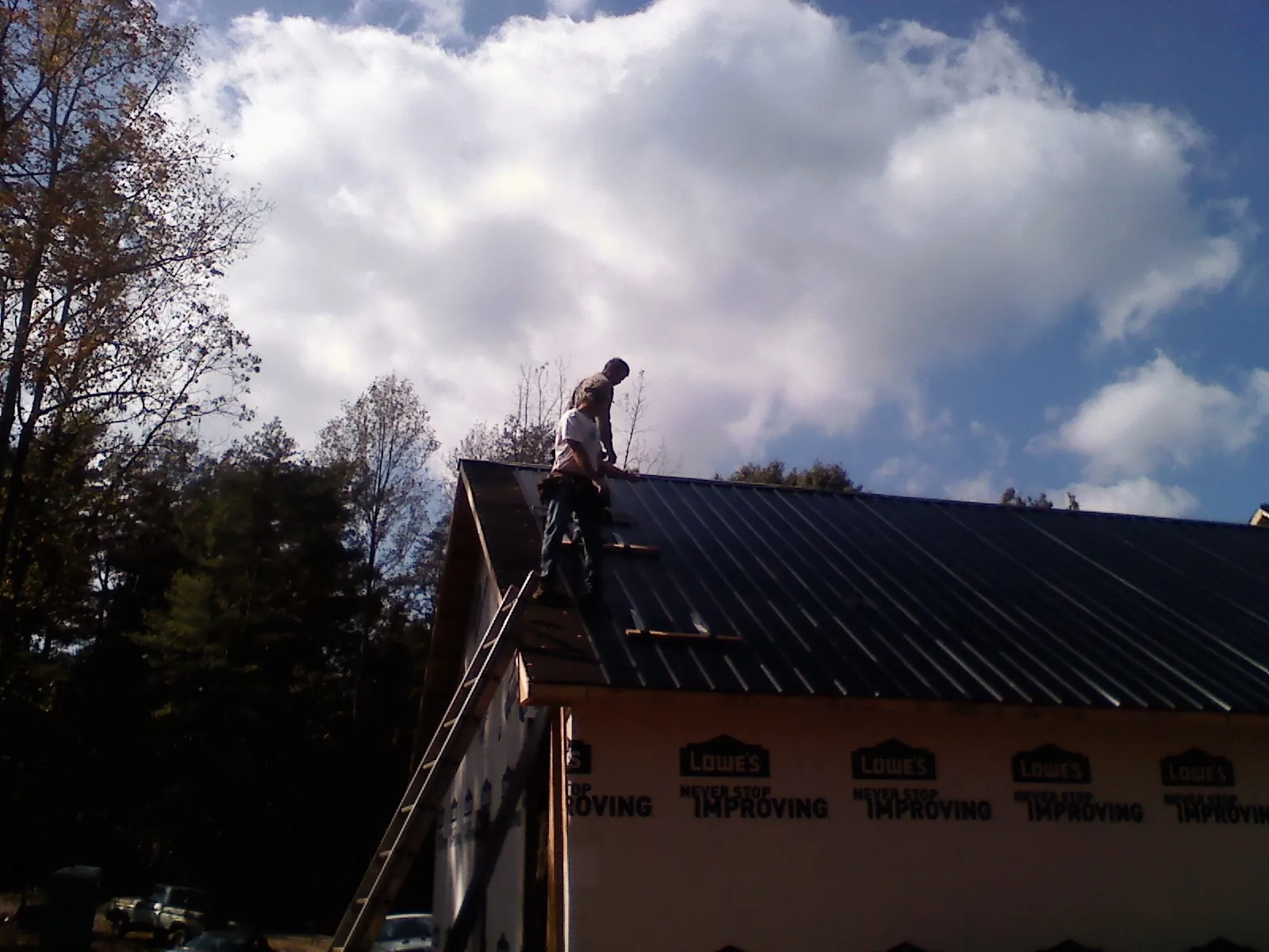 Roofer fastening dark metal panels high against a cloudy sky, from a Roof Inspection job in Moon