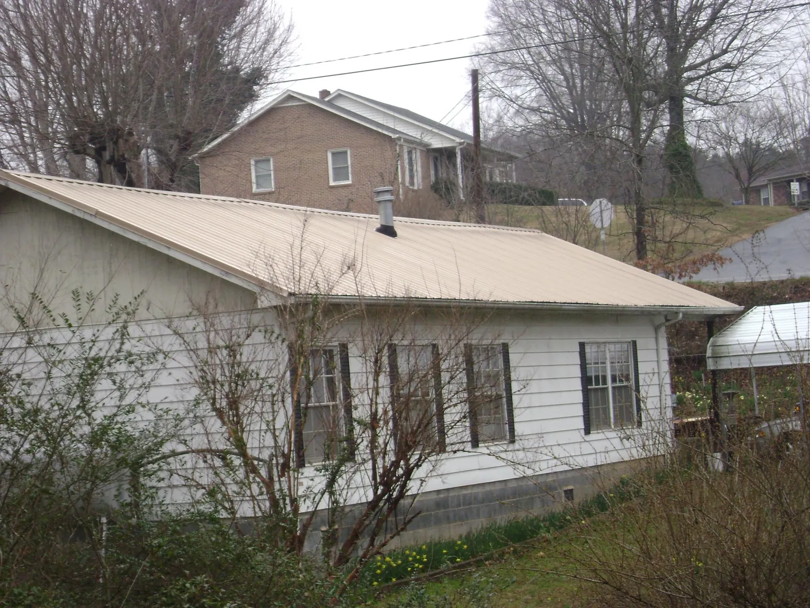 Tan metal roof on a white sided house set into a hillside — Commercial Roofing by Roofing Brothers in Moon